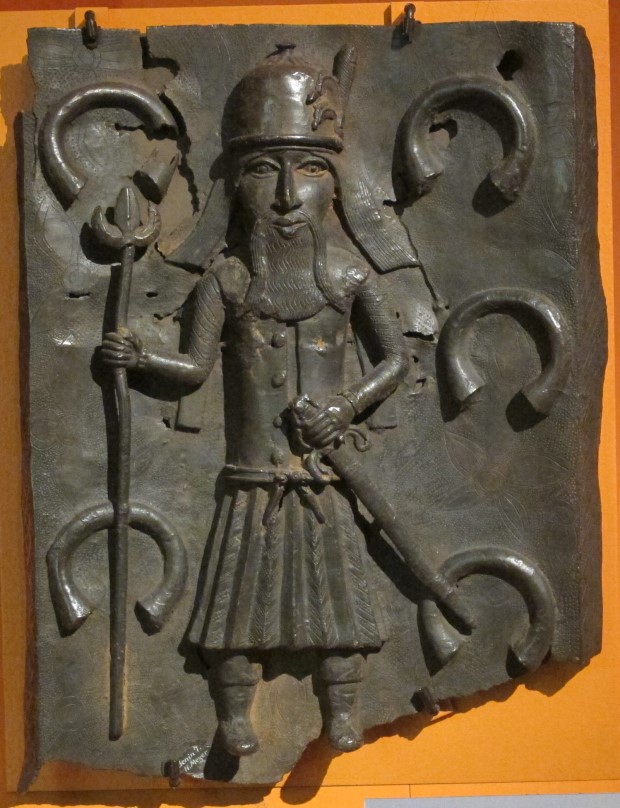A 16th century Benin Bronze depicting a Portuguese soldier with manillas in the background.